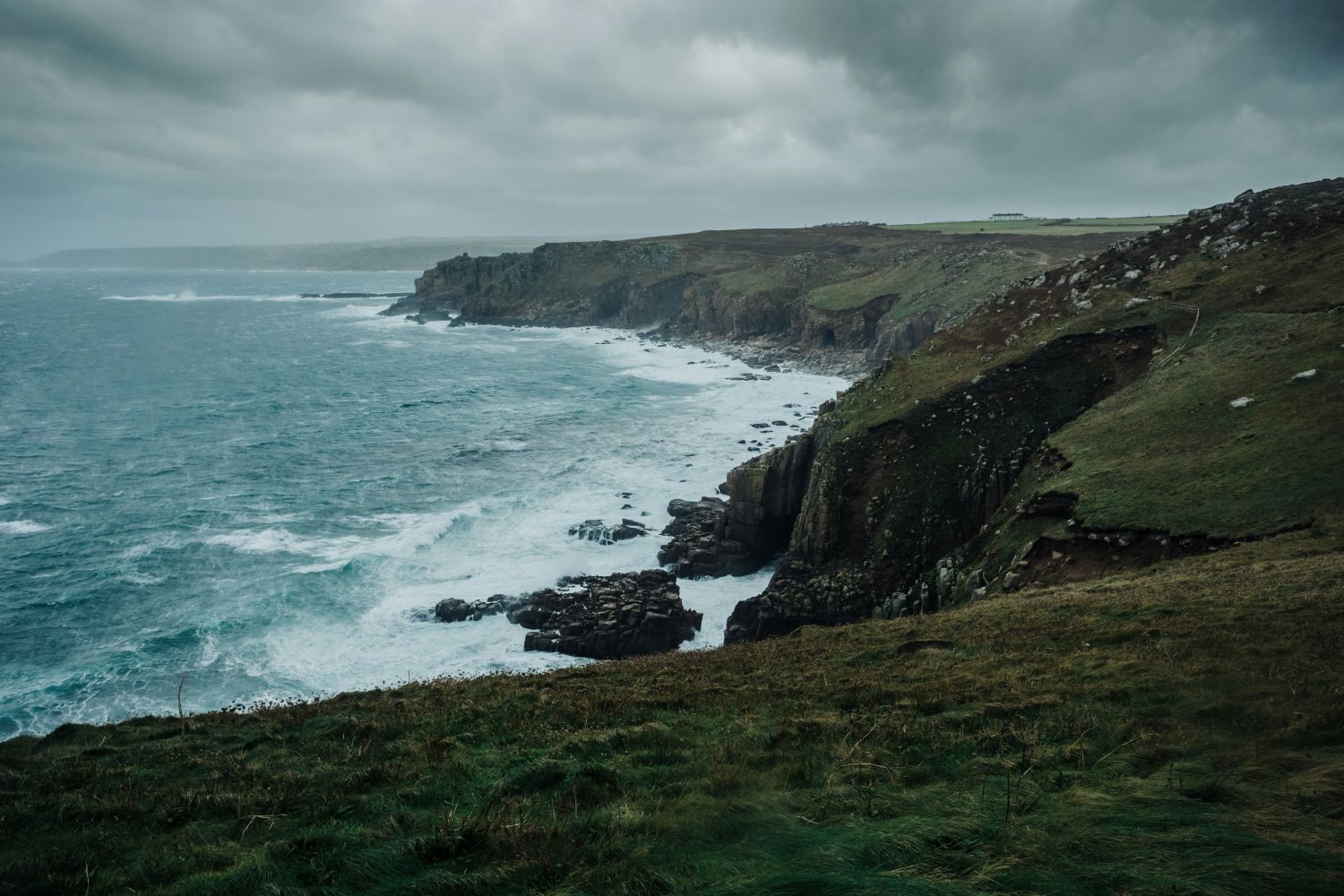 A dramatic coastal landscape with steep grassy cliffs dropping into a turbulent blue-gray ocean under an overcast sky. Books and landscapes