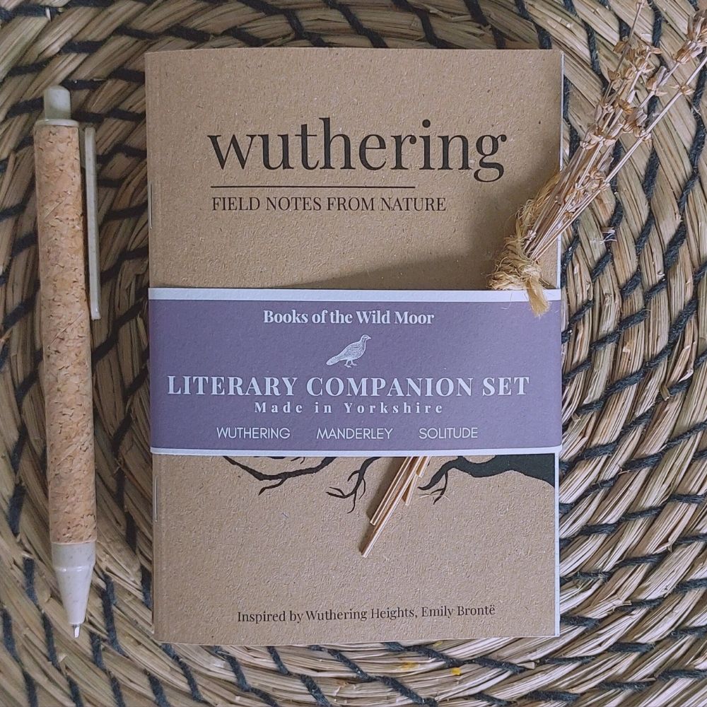 A boxed set of literary companion notebooks titled 'wuthering' from Books of the Wild Moor, placed on a woven straw mat with a cork pen beside it.