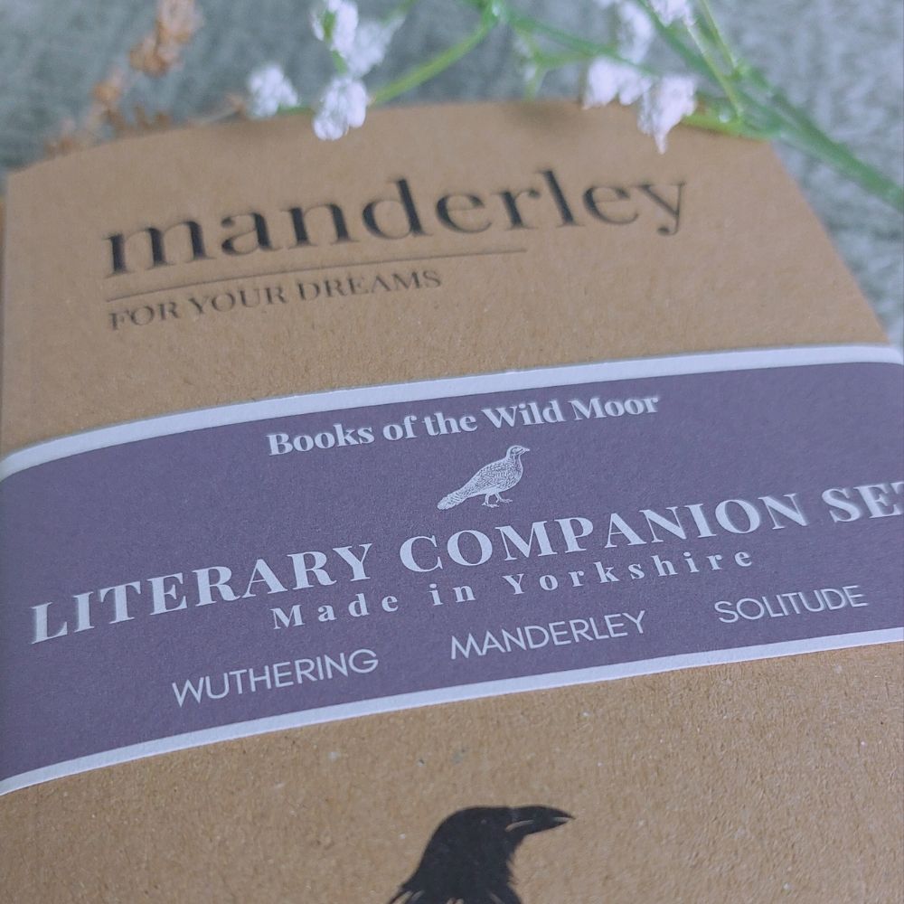 A close-up of a brown paper book cover for the Manderley Literary Companion Set, featuring a dark purple label with white text and a small bird illustration. The cover includes the title 'manderley' and references to Wuthering, Manderley, and Solitude.